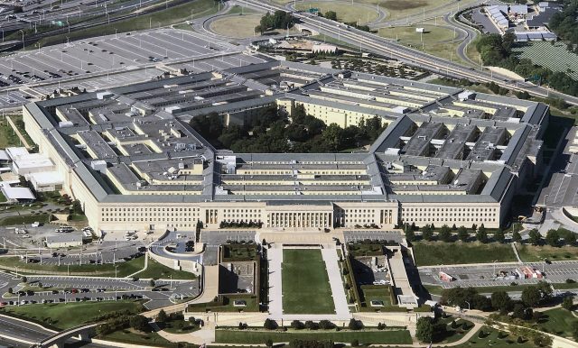 Pentagon Building Rows of labeled file boxes stamped UFO/UAP sit open on a government archive table with a laptop displaying the PURSUE download page.