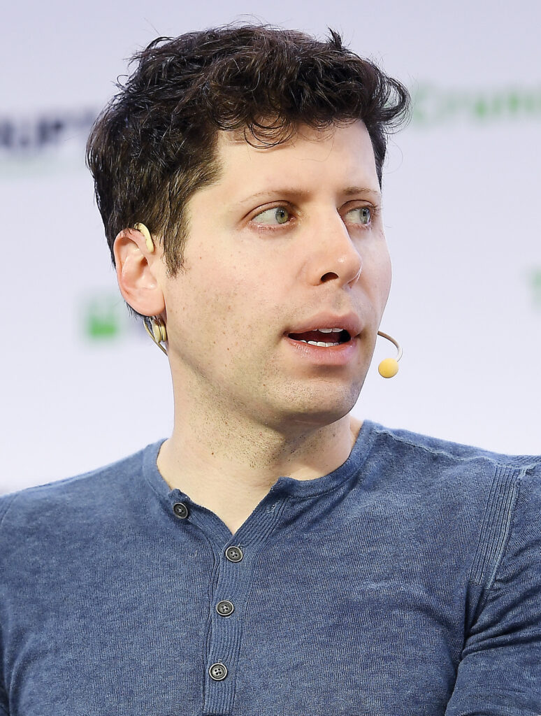 Sam Altman speaking at a technology conference, gesturing while discussing artificial intelligence innovations.